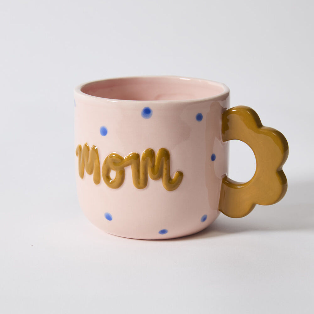 Pink mug with 'mom' text and gold handle on a light gray background