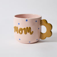 Pink mug with 'mom' text and gold handle on a light gray background