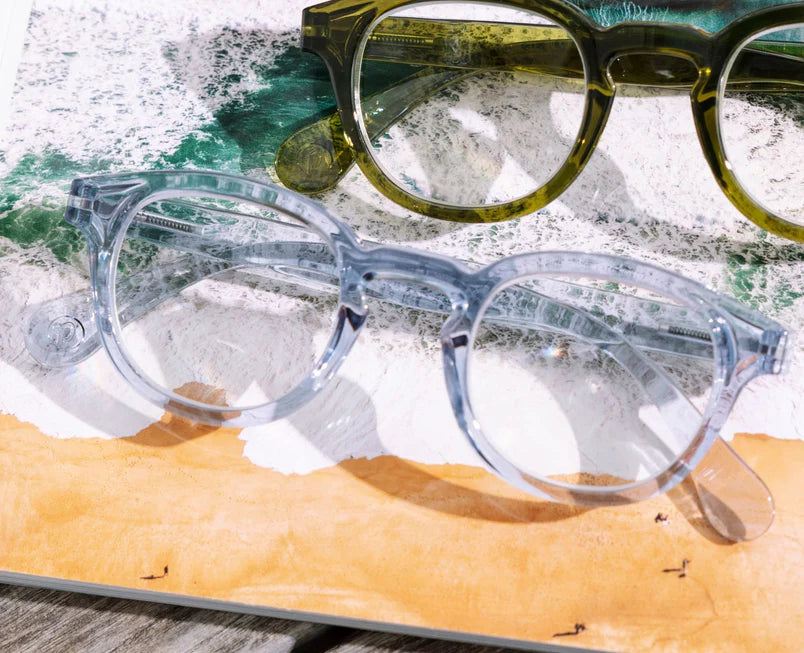 Two pairs of eyeglasses, one clear blue and one green, on a textured surface.