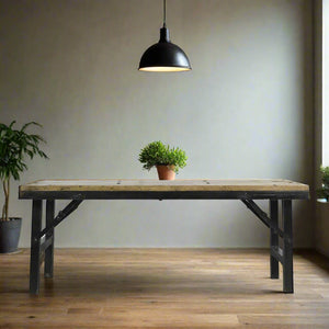 Wooden table with a potted plant under a black pendant light in a room with a neutral wall and wooden floor.