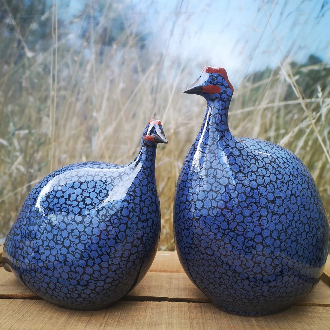 Two blue ceramic guinea fowl with circular accents on a wooden surface with a blurred natural background