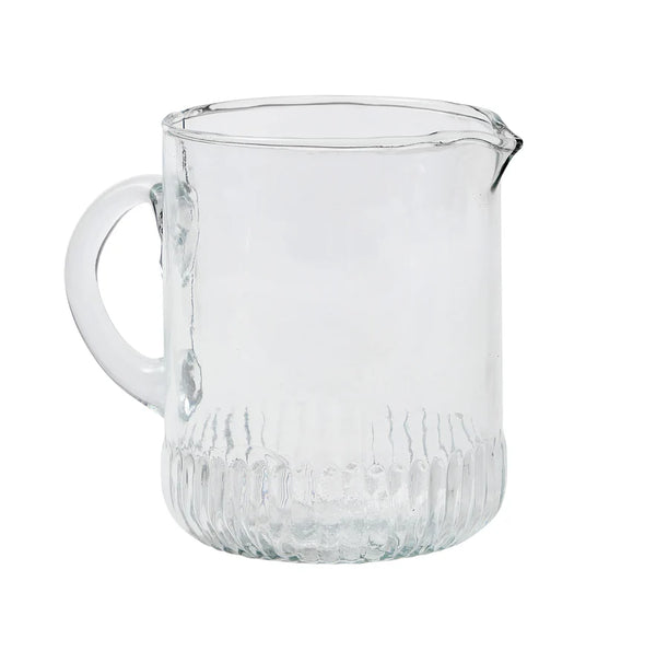 Clear glass pitcher with textured base on a white background