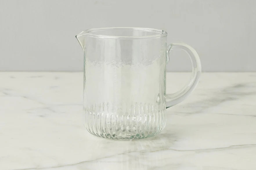 Clear glass pitcher on a marble surface with a gray background