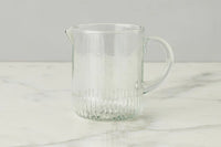 Clear glass pitcher on a marble surface with a gray background