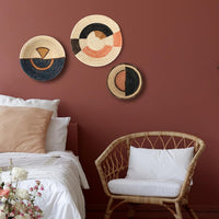 Decorative wall hangings on a red wall above a bed and chair.