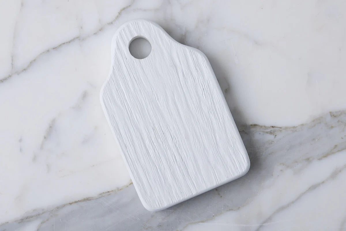 White cheese board with a handle on a marble surface
