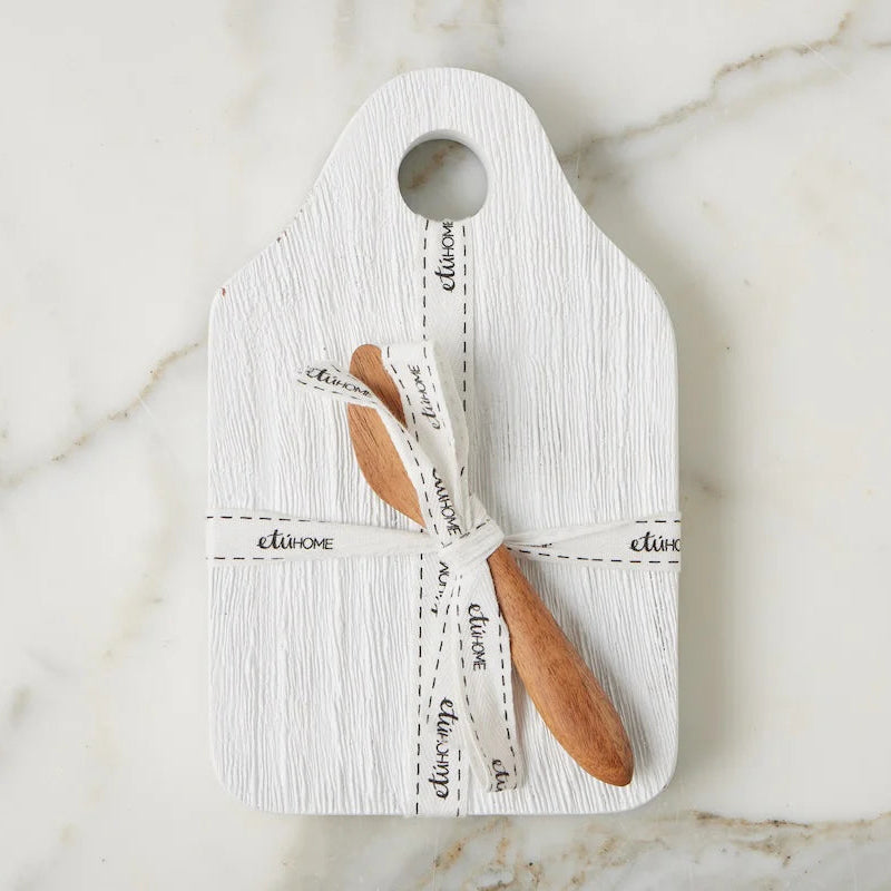 White cheese board with wooden knife and white ribbon on a marble surface