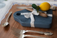 Blue serving board with a lemon and nearby silverware on a wooden surface