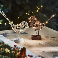 Decorative wire bird lights with string lights on a wooden surface with a festive background.