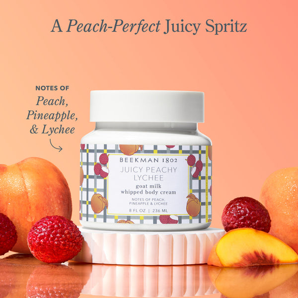 Bottle of Beekman 1802 Juicy Peachy Lychee whipped body cream with peach, pineapple, and lychee elements on a peach background.