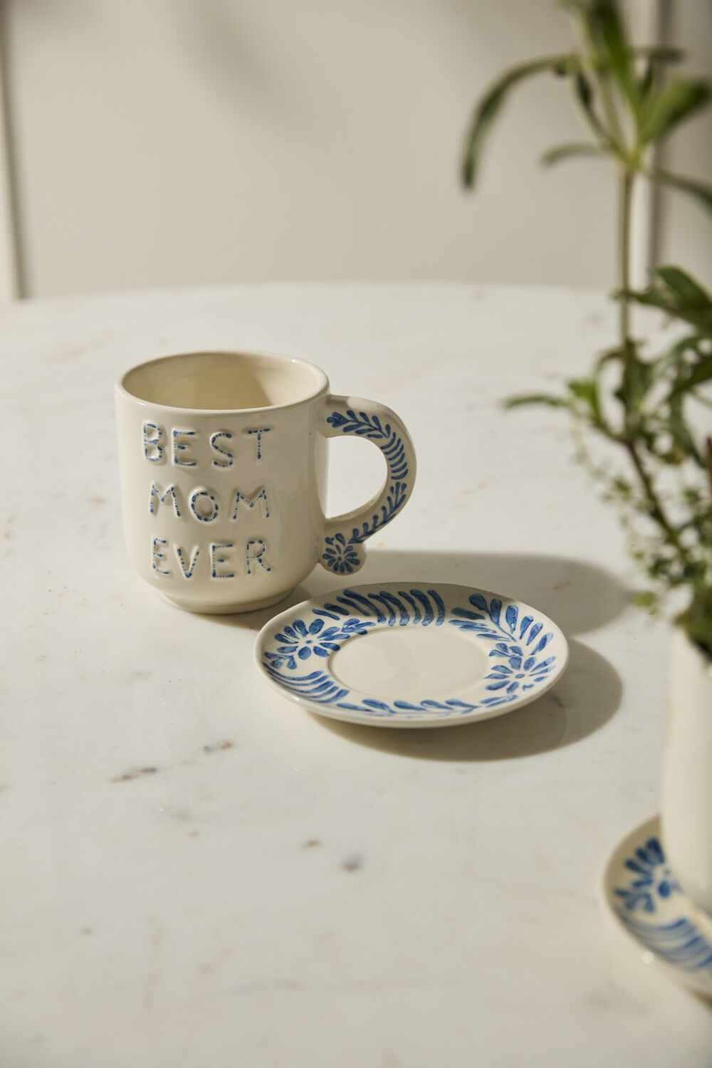 Ceramic mug with 'Best Mom Ever' text on a marble surface with a plant in the background