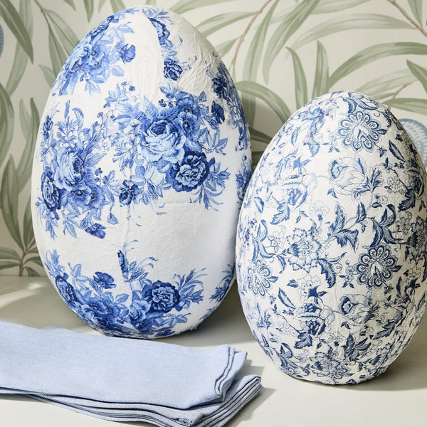 Two decorative eggs with blue floral patterns on a neutral background