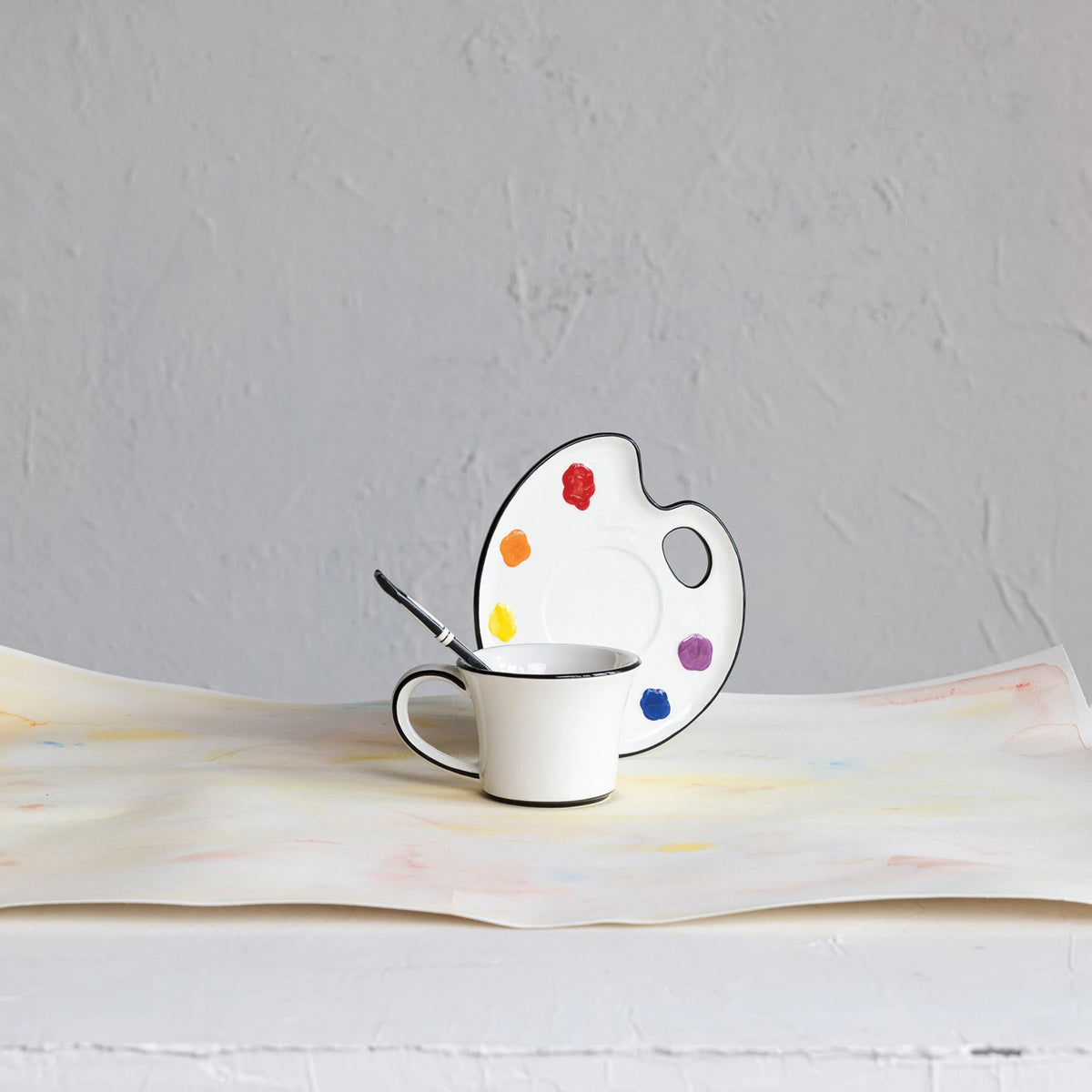 Ceramic cup with saucer shaped like a paint palette on a textured surface