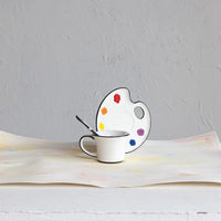 Ceramic cup with saucer shaped like a paint palette on a textured surface