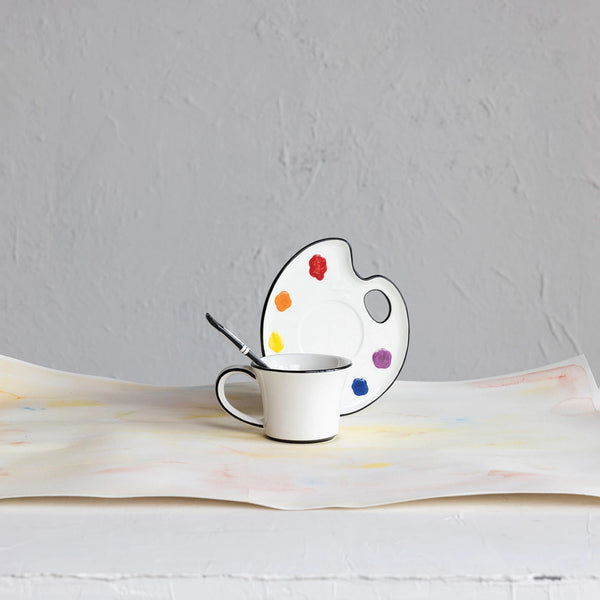 Ceramic cup with saucer shaped like a paint palette on a textured surface