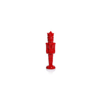 A glossy red nutcracker figurine standing upright on a white reflective surface against a white background.