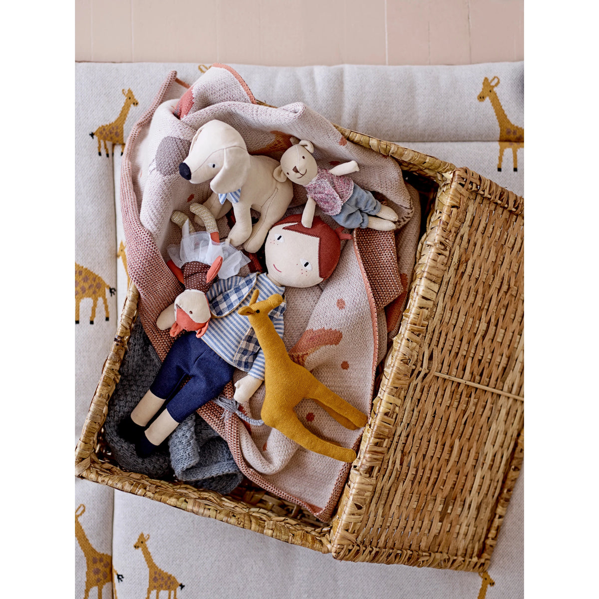 Wicker basket filled with soft toys on a light-colored surface with animal prints.