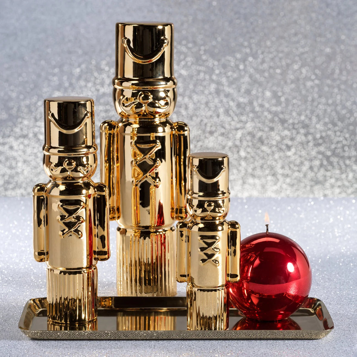 Gold nutcrackers and a red candle on a reflective surface with a silver glittery background