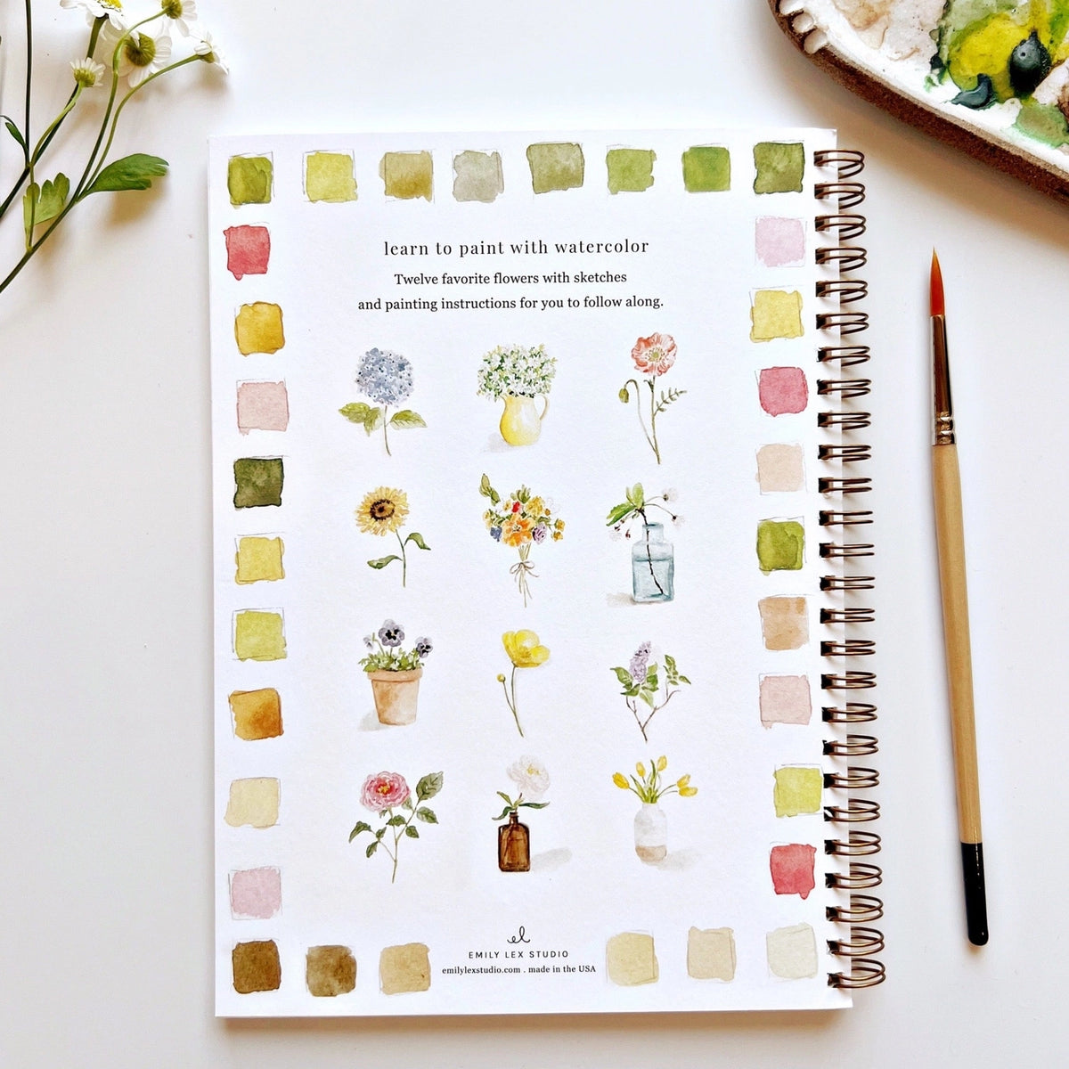 Notebook with watercolor flower illustrations and a paintbrush on a white surface
