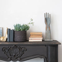 Decorative items on a mantelpiece including books, a plant, and a decorative hand sculpture.