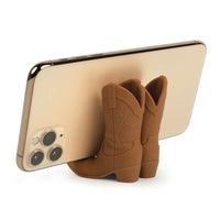 Phone stand shaped like brown cowboy boots with a gold phone on a white background