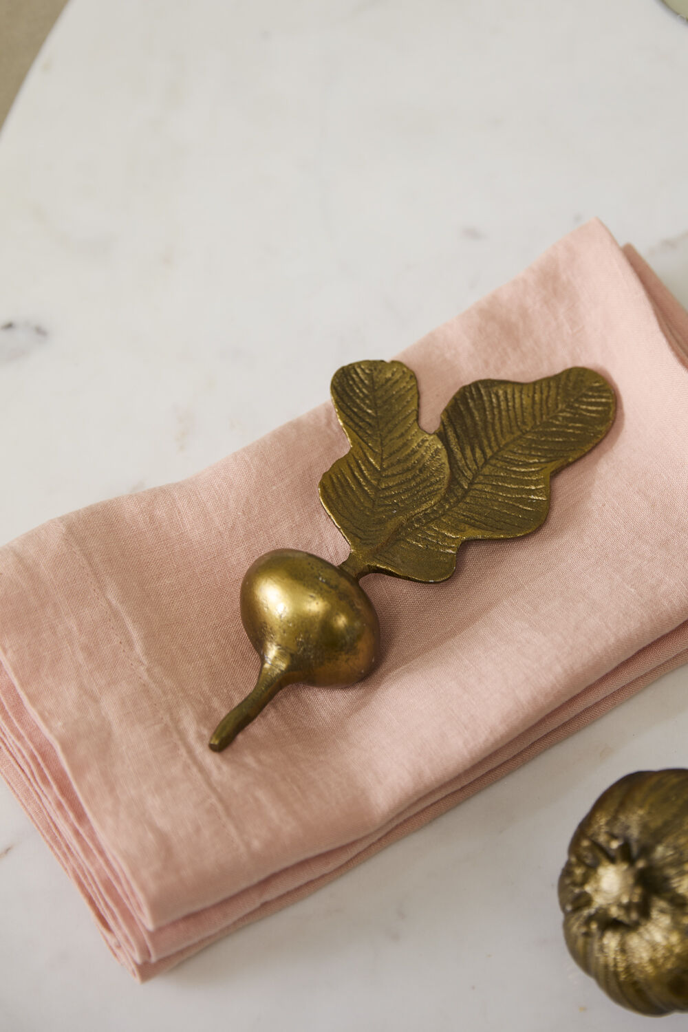 Pink napkin with a gilded metal radish figurine on a light surface.