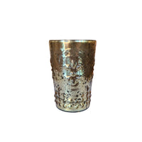 A hammered metallic gold cup with a textured, embossed floral pattern, sitting on a white surface in a blurred shop environment.