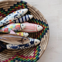 Colorful ceramic fish figurines in a woven basket on a light surface