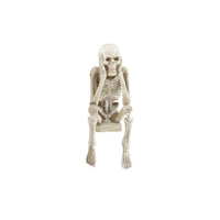 A decorative skeleton shelf sitter with its hands over its mouth in a 'hear no evil' pose on a white background.