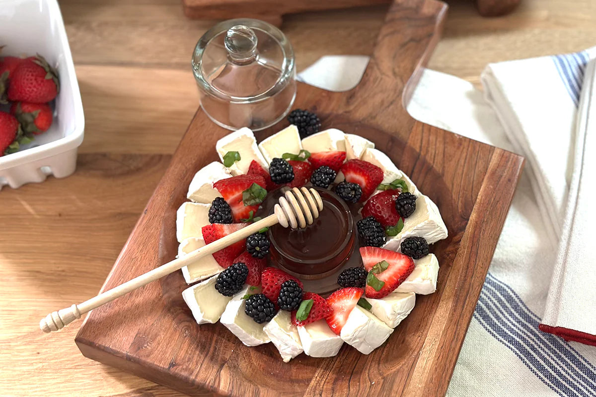 Fruit pizza with strawberries, blackberries, and a honey dipper over a glass container on a wooden board.