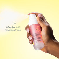 Hand holding a pink bottle of milk shake body mist against a yellow background