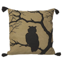 A square decorative throw pillow with a black owl silhouette and bare tree branches on a tan textured fabric background, finished with black tassels at the corners, shown on a plain white background.