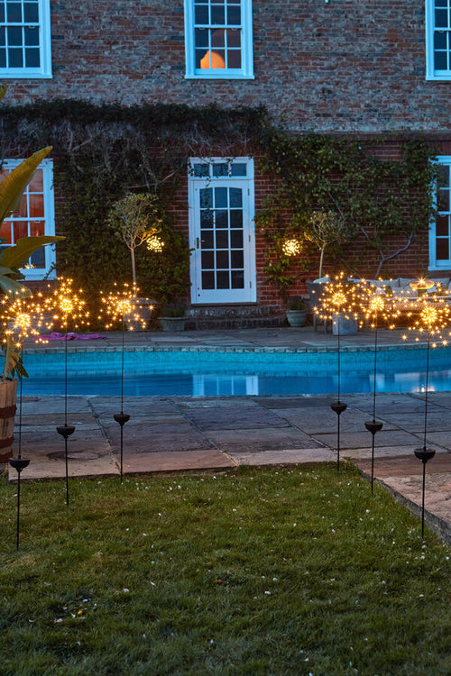 Garden with pool and staked starburst lights in front of a brick building