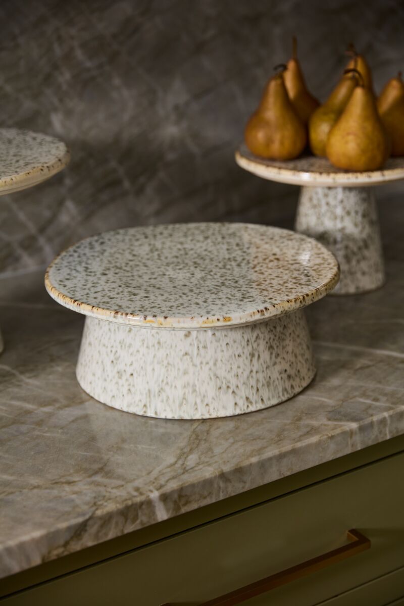 Speckled ceramic cake stand on a marble surface with pears in the background