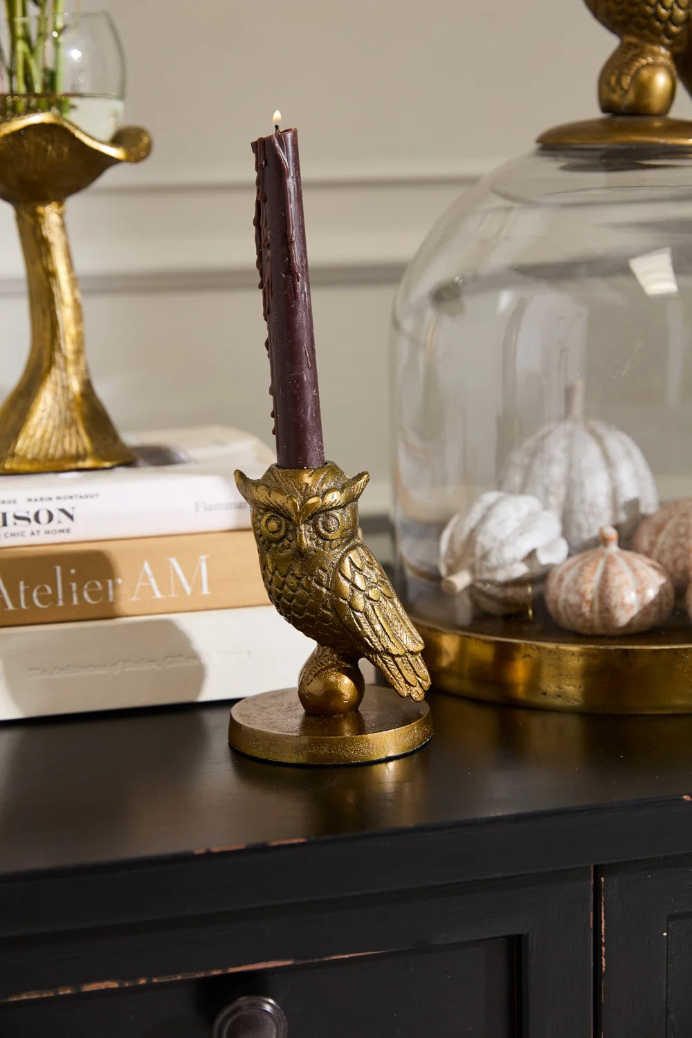 Gold owl candle holder with a purple candle on a dark surface, with books and decorative items in the background.