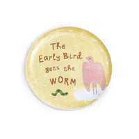 A round decorative plate with a pale yellow background, featuring the text 'The Early Bird gets the WORM' in brown lettering, a pink bird illustration, and a small green worm at the bottom.