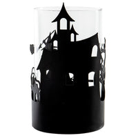A clear cylindrical glass candle holder or vase featuring a black silhouette cutout of a haunted house with bats on the side, shown against a plain white background.