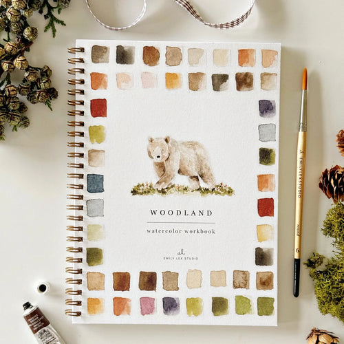 Woodland watercolor workbook with a bear illustration on a white surface with decorative items.