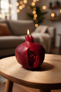 A pomegranate-shaped candle with a lit flame on a wooden table with a blurred living room background.