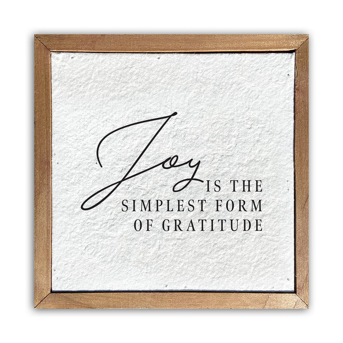 A white rectangular pulp paper wall sign with the words 'Joy' and 'Gratitude' written in a simple black font, surrounded by a gold-colored wooden frame.