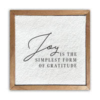 A white rectangular pulp paper wall sign with the words 'Joy' and 'Gratitude' written in a simple black font, surrounded by a gold-colored wooden frame.